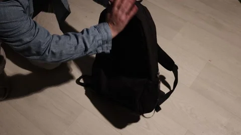 Person's hands adjusting a black backpack on a wooden floor Stock Footage 339176738