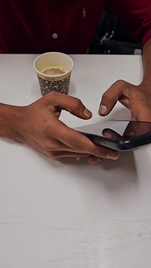 A persons hands are actively engaging with a smartphone, with a cup Stock Footage 311765547