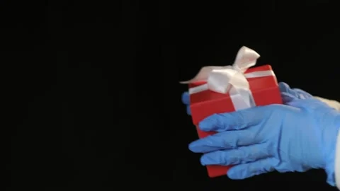 Person's hands in blue protective gloves giving red gift box with white ribbon Stock Footage 144086911