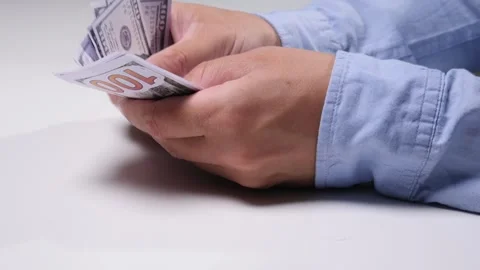 Person's hands carefully counting a stack of hundred dollar bills, representing Stock Footage 342761511