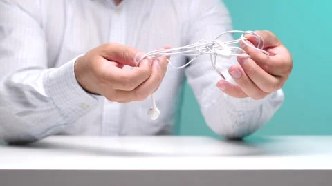 Person's hands carefully manipulating a knot of white tangled earphones Stock Footage 342760464