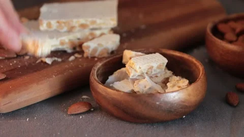 A person's hands carefully put pieces of hard white almond turron into a wood Stock Footage 331378892