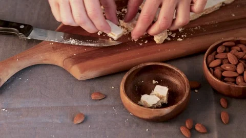 A person's hands carefully put pieces of hard white almond turron into a wood Stock Footage 331378968