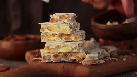 A person's hands carefully put pieces of hard white almond turron into a wood Stock Footage 331379253