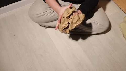 Person's hands crumpling brown paper packaging on a light wood floor Stock Footage 339175900