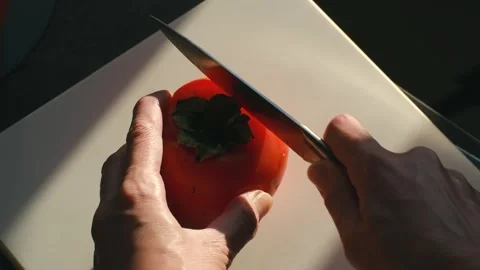 Persons hands cutting fresh ripe persimmon on white cutting board Stock Footage 324773703