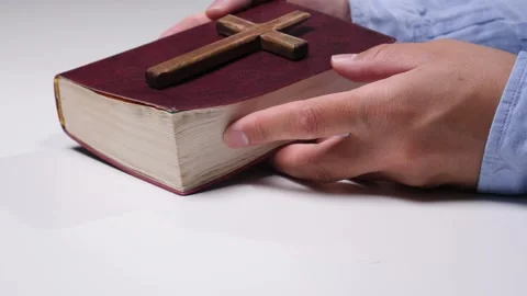 Person's hands gently resting on a closed red holy bible with a rustic wooden 動画素材 342769448