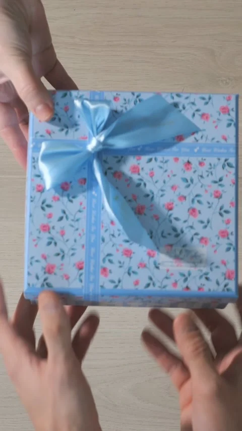 Persons hands giving and receiving a beautiful floral gift box with a blue Stock Footage 341677313