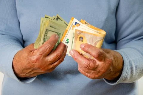 A persons hands holding a stack of US dollar bills and a stack of euro bills Stock Photos