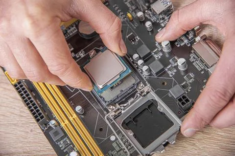 A persons hands installing a silver processor chip into the socket of a computer 스톡 사진