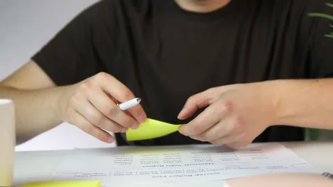 A persons hands jot down ideas or reminders on a sticky note while referencing a Stock Footage 316765920