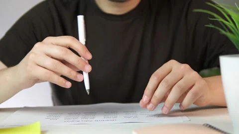 A persons hands pause over a document with a table, then mark it with a pen Video stock 316751614