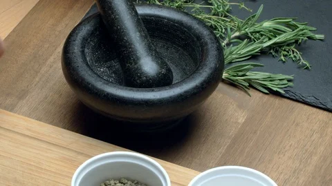 Person's hands putting peppercorns into a dark stone mortar and pestle Stock Footage 97410179