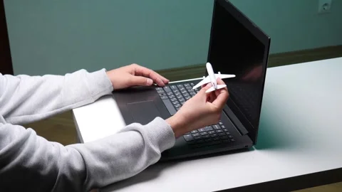 Person's hands typing on a laptop keyboard while holding a small white airplane Stock Footage 345170140