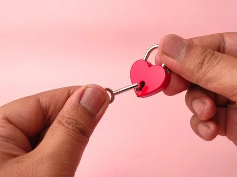 A person's hands use a small key to unlock a red heart-shaped padlock over .. 库存照片