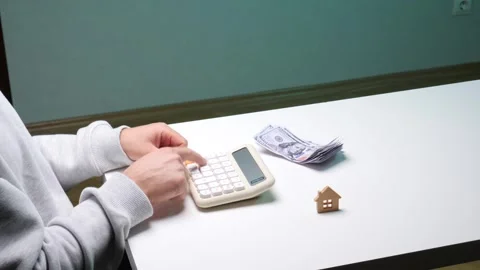 Person's hands using a calculator on a white desk with a stack of hundred Stock Footage 346251379