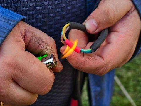 Persons hands using a gas lighter to apply heat to red heat shrink tubing Stockfoto's