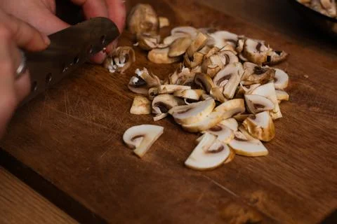 Persons hands using a knife slicing fresh raw champignon mushrooms on a rustic Stock Photos