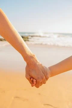 "persons holds hands on beach with waves in background during afternoon..Two Stock Photos