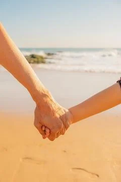 "persons holds hands on beach with waves in background during afternoon..Two Stock Photos