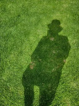 Person's shadow stretching across green grass field Stock Photos