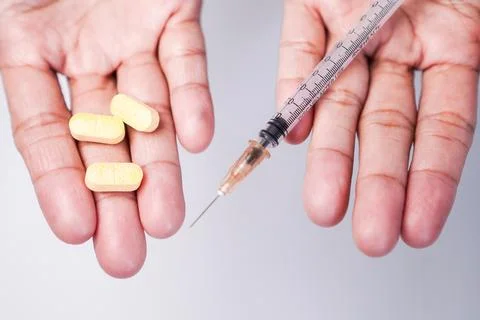 A person's three yellow oblong tablets in the left palm and a plastic syrin.. Stock Photos