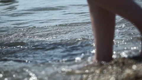 Persons walking barefoot on pebbly beach edge, small waves washing over feet Stock Footage 335763620