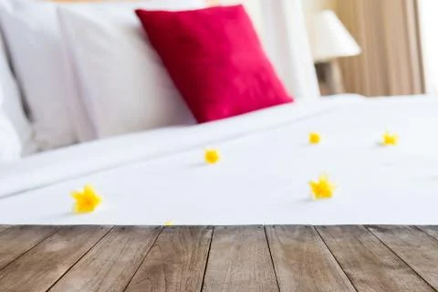 Perspective empty wooden table in front of hotel bed with flowers Stock Photos