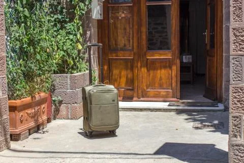 Perspective front shot of suitcase in front of masonry hotel in Greece Foto stock