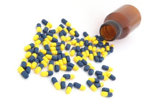 Perspective of open pill bottle with capsule spilling out of it Stock Photos