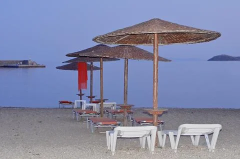 Perspective row of straw umbrellas and sunbeds on a peaceful beach at sunset Stock Photos