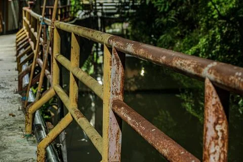 Perspective of rusty industrial iron railing on canal walkway near midnig Фото