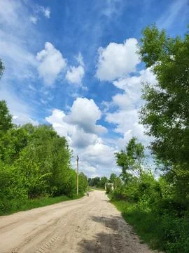 Perspective view of a forest road under a blue cloudy sky, summer journey Stock Photos