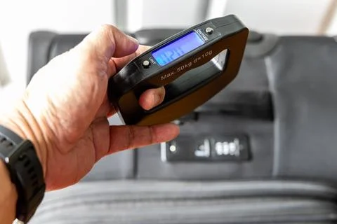 Perspective view of hand holding digital weighing scale to ascertain luggage Stock Photos