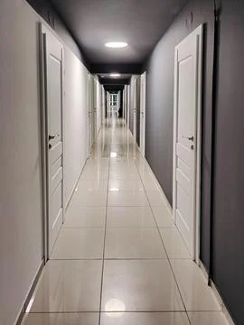 A perspective view of a long office corridor brightly lit by lamps Stock Photos