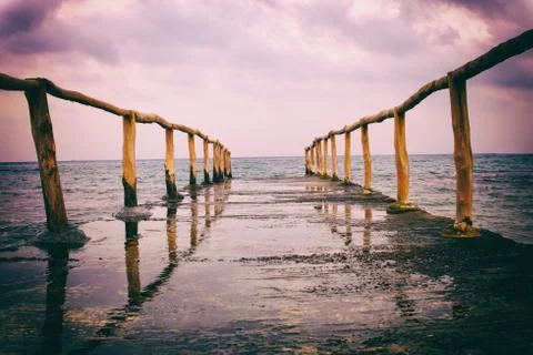 Perspective view of a pier on the seashore with clear blue sea and dramatic s Stock Photos