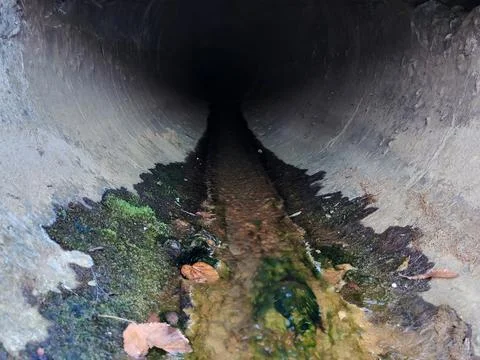 A perspective view of a sewer pipe from which sewage flows Stock Photos