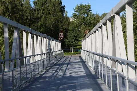 A perspective view walking across a modern pedestrian metal truss bridge lead Stock Photos