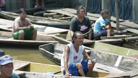 Peruvian men operate a motor engine sailing on a wooden boat, on a dirty river. Stock Footage 197073899