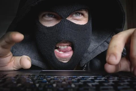 Pervert maniac or hacker sits in the dark at a computer and looks at the screen 库存照片