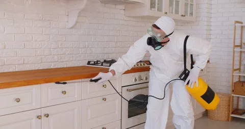 Pest control worker in protective suit spraying insecticide on kitchen cabinets Stock Footage 326062130