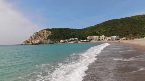 Petrovac Beach waves rolling onto sandy Adriatic shoreline with coastal village Stock Footage 336581772