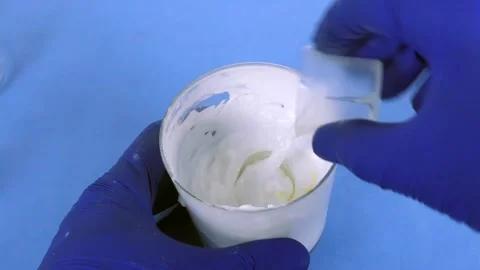 Pharmacist in blue gloves mixing a white emulsion with a yellow liquid in a Vidéo 335183087