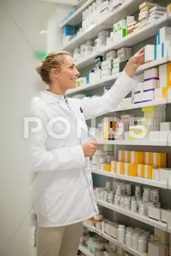 Pharmacist Browsing Medicines On Shelf
