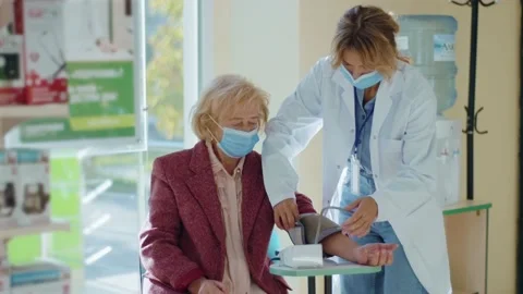 Pharmacist checking blood pressure of old woman customer with mask in pharmacy Stock Footage 140763858