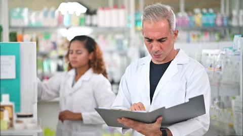 Pharmacist holding clipboard checking inventory in drug store Stock Footage 132586457