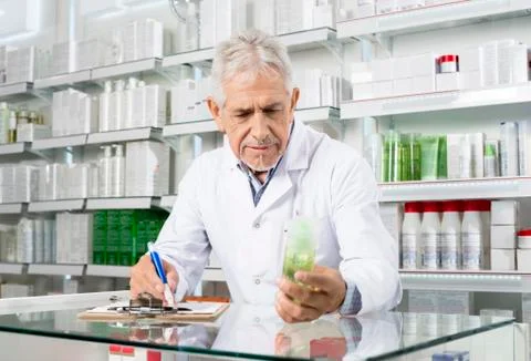 Pharmacist Holding Product While Writing On Clipboard Stock Photos