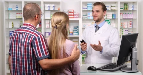 Pharmacist Man Presenting to Young Couple New Drug Medicine Talking in Pharmacy Stock Footage 80281025