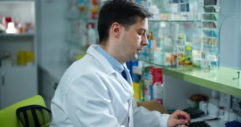 A pharmacist man sits in a pharmacy on the background of drugs. Stock Footage 133083147