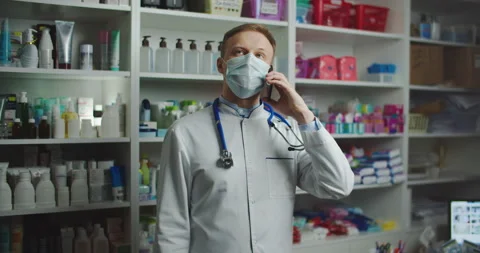 A pharmacist with a medical mask at a pharmacy advises a client by phone Stock Footage 144351153
